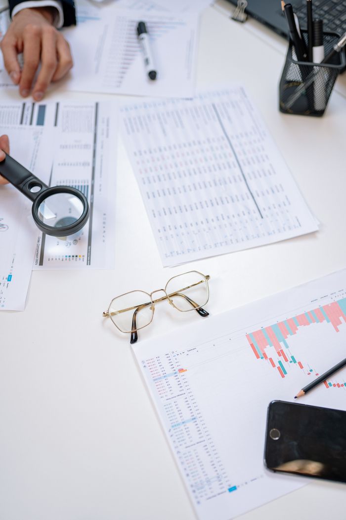 Flat lay of business documents with magnifying glass, glasses, and smartphone on a desk.